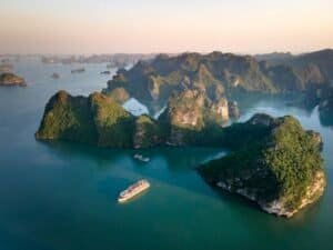 Ha Long Bay limestone islands and traditional boats under sunset.