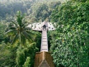 A breathtaking view of a treetop walkway leading to a thatched-roof building amidst a dense jungle, Bali