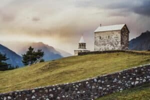 A serene landscape featuring a historic church against the backdrop of the Kazbegi mountains at sunset, Georgia