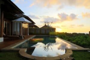 A serene view of a villa's infinity pool at sunset in Bali, Indonesia, with lush greenery and calm reflections
