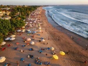 Aerial shot of lively beach with colorful umbrellas and ocean waves in Seminyak, Bali