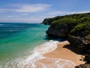 Explore a stunning tropical beach with turquoise waves golden sand and lush green cliffs Bali Bali Budget Travel Guide 2026: Travel Bali Cheap Under $50/Day Explore a stunning tropical beach with turquoise waves, golden sand, and lush green cliffs, Bali